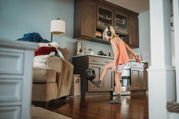 Young girl balancing soccer ball on foot indoors watching iPad