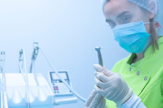 Woman dentist with mask and gloves preparing the drill, dental clinic