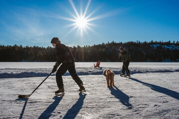 Father and son playing hockey on outdoor rink on frozen Canadian lake.