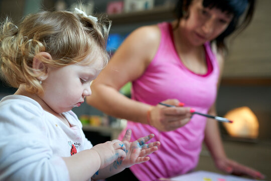 Cute little girl looking at her painted hands with her mother in background