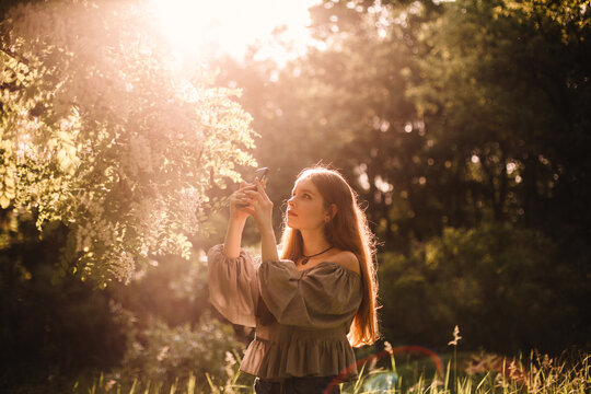 Teenage girl photographing flowering tree with smart phone in summer