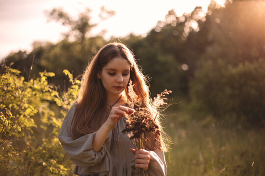 Teenage girl holding bouquet of dried flowers standing on summer field