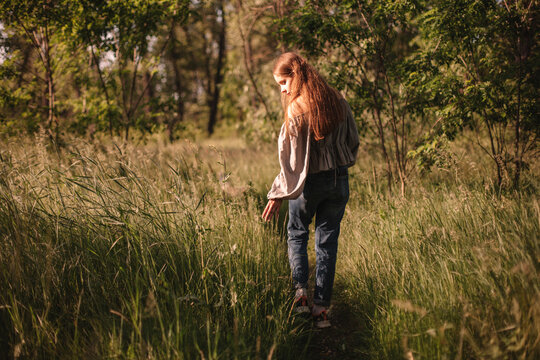 Back view of teenage girl touching grass walking on path in summer