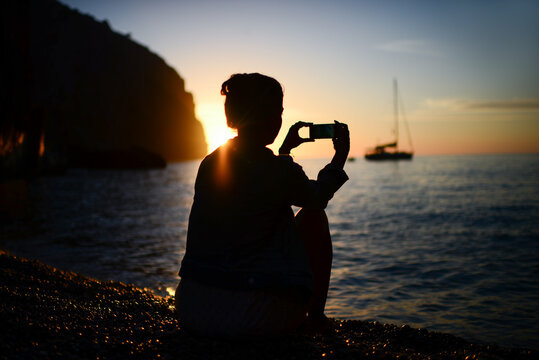 Silhouette of a young woman using a smartphone to capture sunset