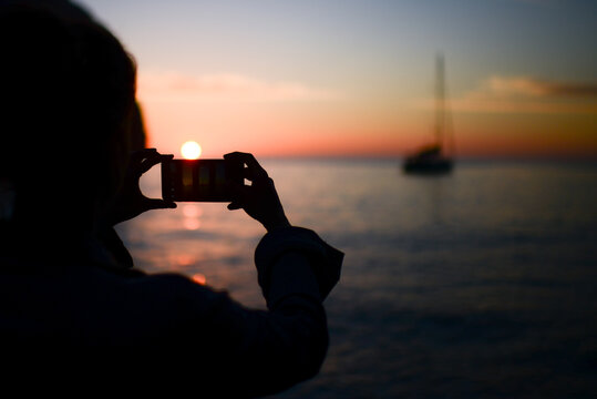 Silhouette of a young woman using a smartphone to capture sunset