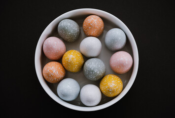 Colorful Easter eggs in white bowl on black background