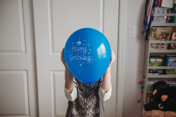 Tween girl holding blue birthday balloon in front of face