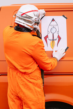 Man disguised as an astronaut sticks a poster with a drawing of a rocket on the van