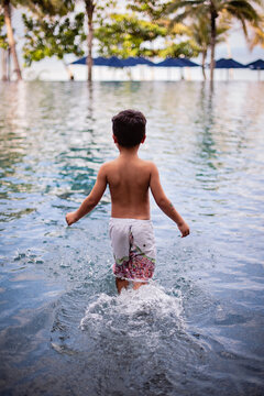 Boy walking into an infinity pool in a tropical setting.