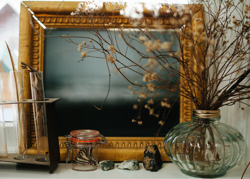 A window ledge holds framed art, flowers, feathers, rocks, stones, and a butterfly