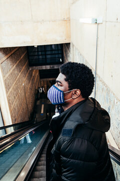 Portrait of black afro american boy with face mask going down escalator.