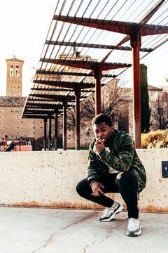 Portrait of an Afro-American boy dressed in military jacket squatting in an urban park.