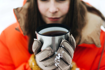 Woman  in orange jacket drinking hot tea outdoors in winter.