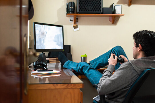 Young man in sweatshirt and jeans relaxing playing video games in his bedroom.