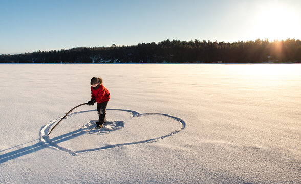 Child drawing a heart shape in an open snowy field in the morning sun.