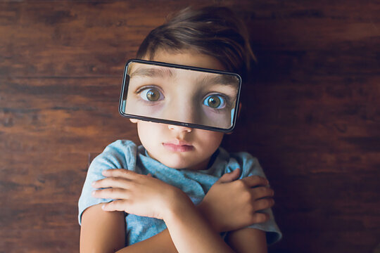 Boy laying on the ground with a phone photo of his eyes on top of face