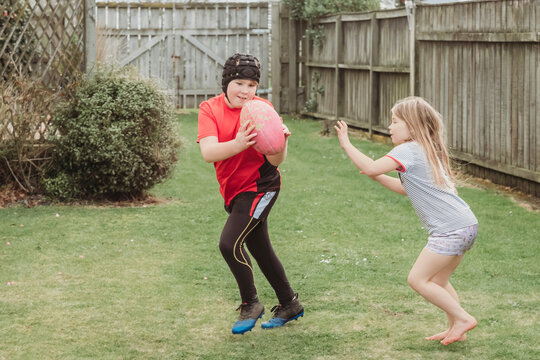 Young brother and sister playing with rugby ball in backyard