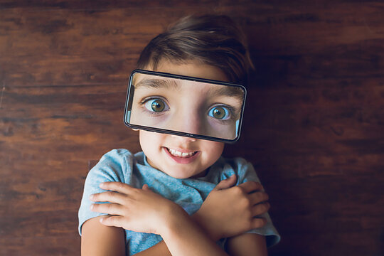 Boy laying on the ground with a phone photo of his eyes on top of face