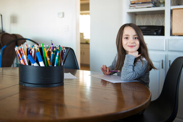 Little Girl Sitting at a table with paper and pencil.