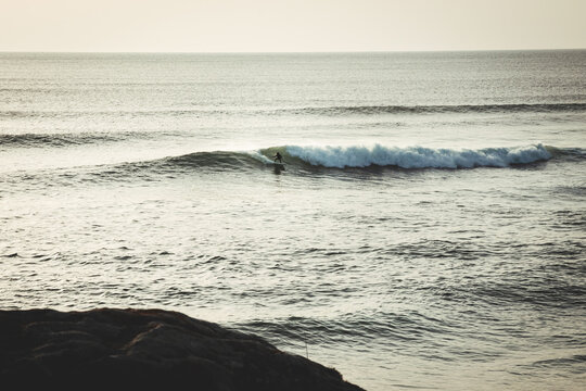 Man surfing a wave alone at sunset with a rock in the foreground