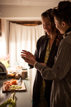 Queer couple smile and follow recipe on device while cooking dinner