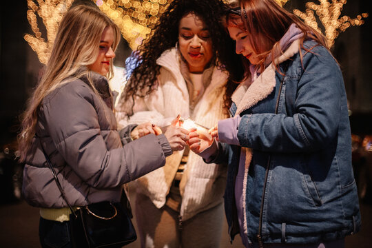 Female friends igniting sparklers standing in city during Christmas