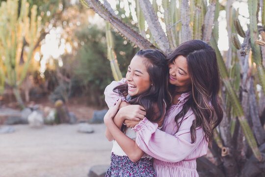 Asian mother hugging pre-teen daughter and making her laugh.