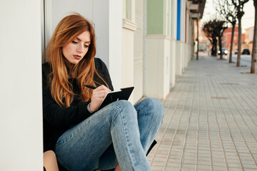 Young woman writes in her notebook while she is sitting on the street