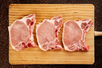 Top view of three raw pork chops on a wooden cutting board
