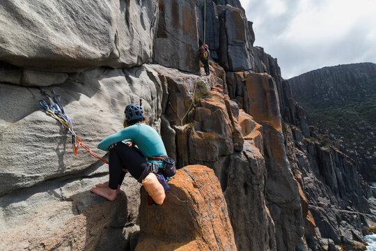 A couple of explorers uses their ropes to rappel and rockclimb while on an adventure on the blocky sea cliffs of Cape Raoul on a cloudy day, in Tasmania, Australia.