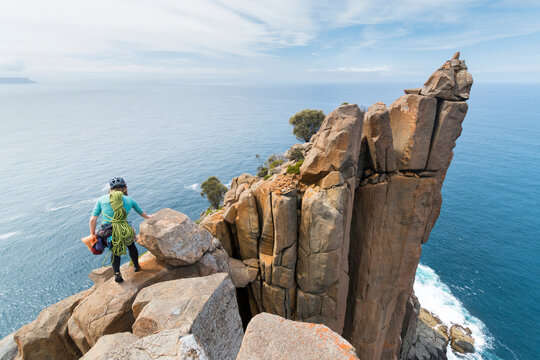 Female adventurer heads off into the unkown, armed with ropes and climbing gear, as she explores dolerite rock columns in the  sea cliffs of Cape Raoul, in Tasmania, Australia.
