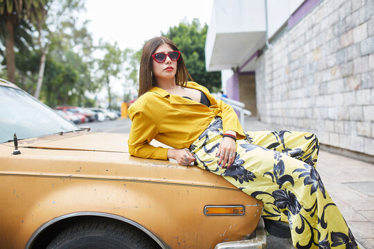 confident young woman leaning on a car and looking at the car