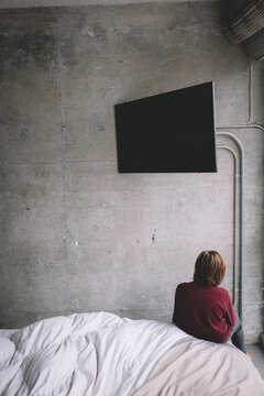 Boy faces concrete wall with blank TV looming over his head.