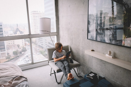 Boy Works on iPad from a hotel room in the City