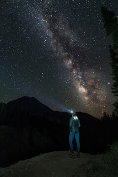 Woman with head lamp standing by Copper Lake against star field at night