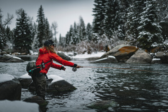 Side view of female fly fishing while standing on snow covered rock by river during winter