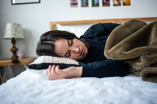Woman lying sideways on bed under blanket