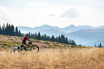 Side view of young woman cycling by dog on field against sky during vacation