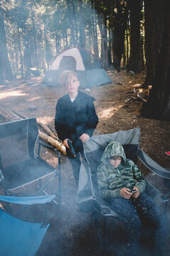 Two Boys by a campfire in the woods with a phone and a BB Gun.