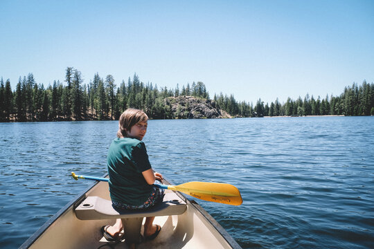Boy in Canoe on a deep blue with a yellow oar.