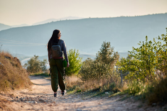 A female explorer walks along a dirt road observing nature