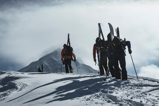 Rear view of people with backpacks and splitboards on snowcapped mountain against cloudy sky