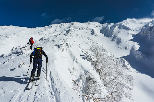 Low angle view of people with splitboards and backpacks climbing snowcapped mountain