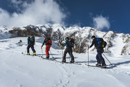 Men with backpacks splitboarding on snow covered mountain against sky during vacation