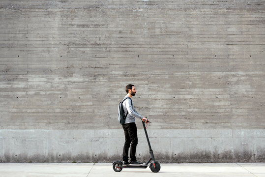 Man riding electric scooter in front of grey wall - Powered by Adobe