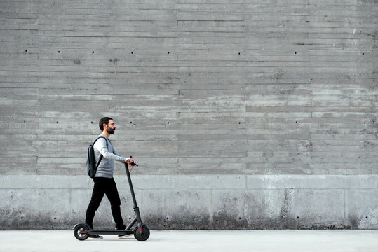 Man walking near electric scooter in front of grey wall