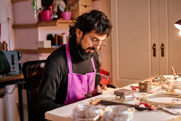 Jeweler craftsman cutting a metal plate with a saw at the work table inside the workshop