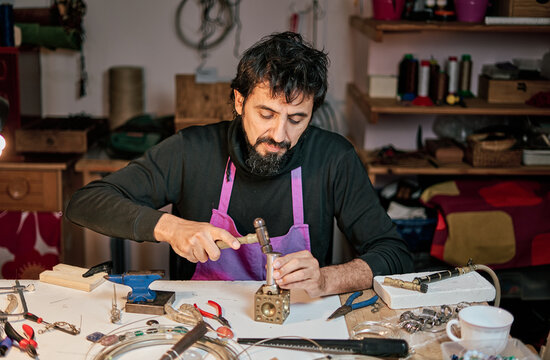 Jeweler craftsman hitting a metal plate with the hammer on the work table inside the workshop