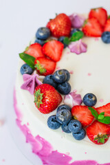 Delicate cake garnished with fresh strawberries blueberries on a pink plain background. Festive dessert with berries