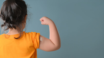 Little asian girl with bandage plaster on her arm after Covid-19 vaccination. Injection covid...